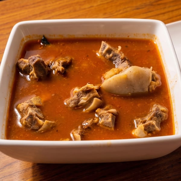 Close-up of a white square bowl filled with a rich red stew and chunks of meat.