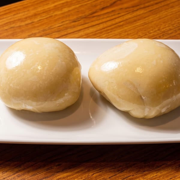 Two light-colored, smooth, round dumplings sit on a white rectangular plate on a wooden table.